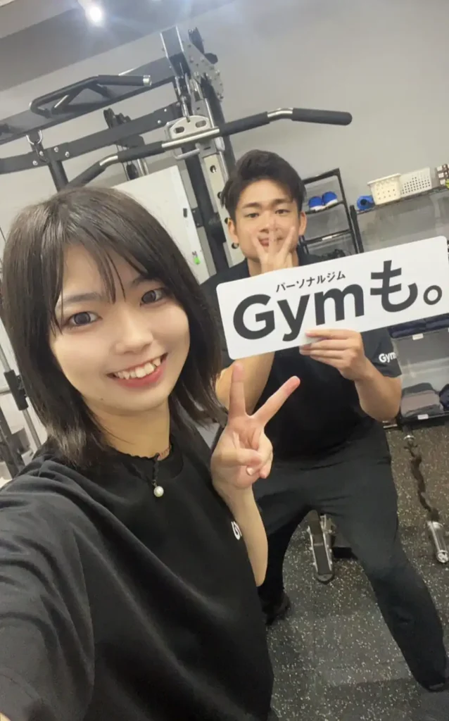 パーソナルジム「Gymも。」の店内で、笑顔の女性スタッフと男性トレーナーが写るセルフィー写真