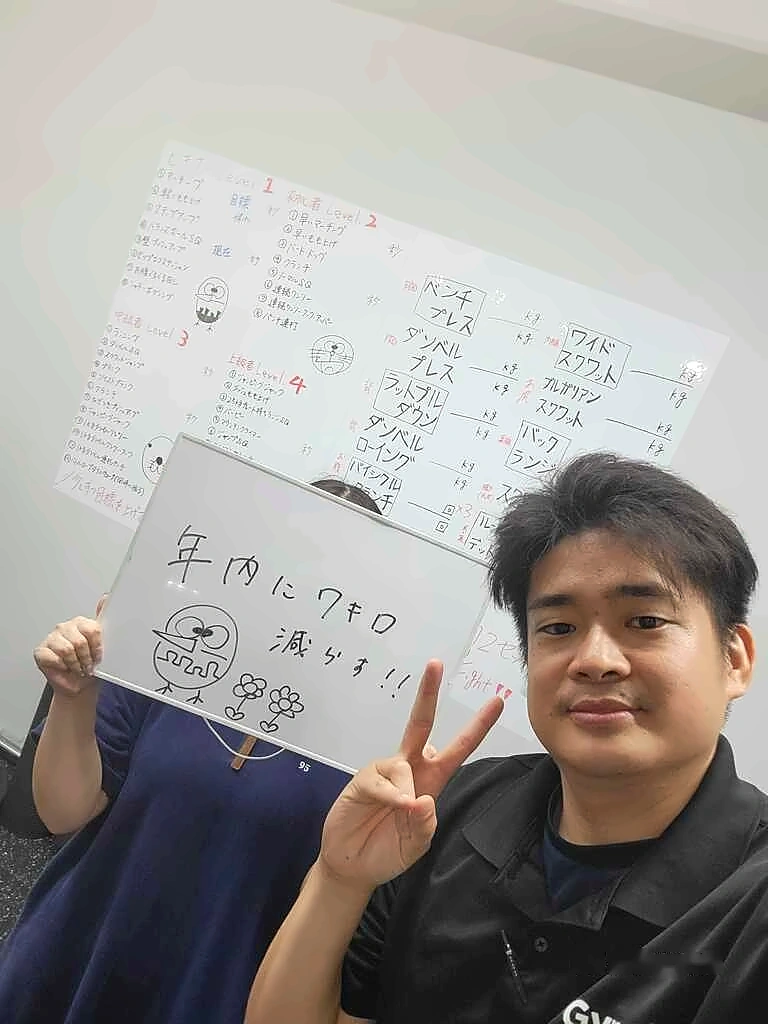 HaneGymのパーソナルジムで「年内に7キロ減らす!!」と書かれたボードを持つ会員とピースサインをするトレーナー