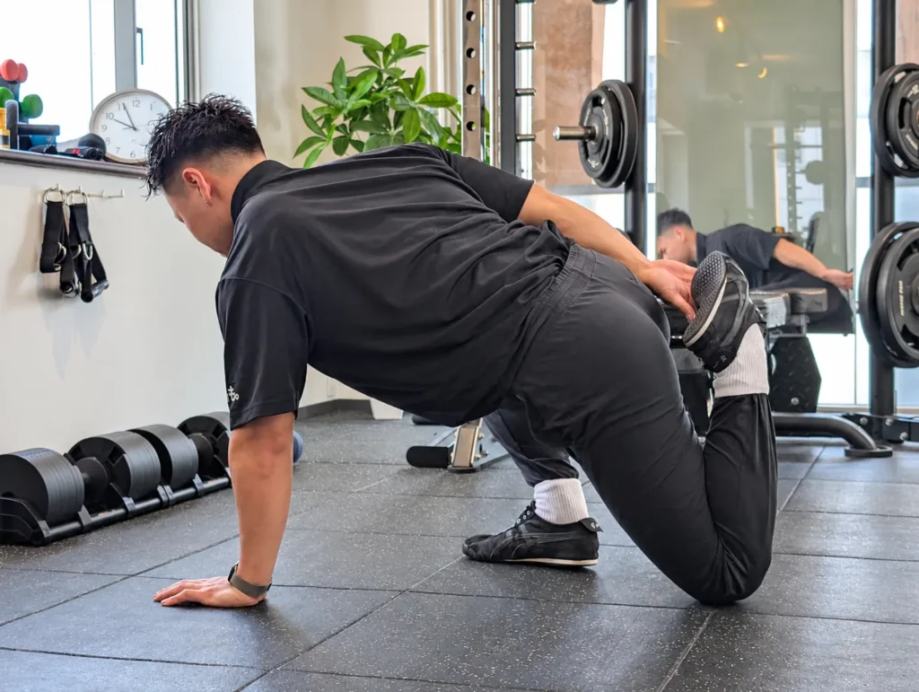 Gymも。の小川トレーナーが、片膝をついて後ろ足を手で持ち、太ももの前側を伸ばす様子