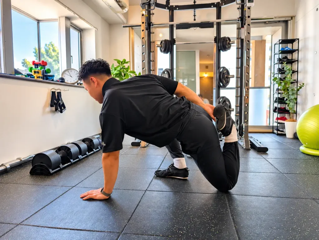 Gymも。の小川トレーナーが、床に両手をついた姿勢で股関節まわりをほぐす様子